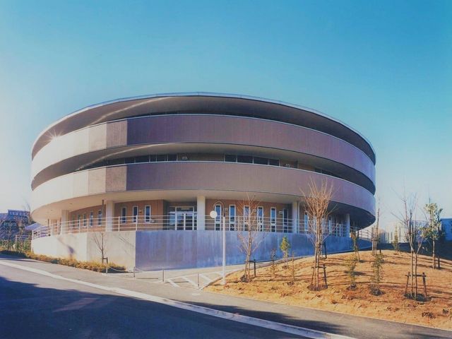 円形の建物外観 外観   曲線を活かした外観で、明るい空の下にすっきりとした印象です。周囲には植栽があり、ゆったりとした雰囲気が感じられます。