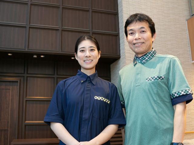 笑顔のスタッフ2人とロビー ロビー   落ち着いた色合いの壁面を背景に、笑顔のスタッフ2人が並んで立っています。来訪時の印象を大切にしたい職場に向いていそうです。