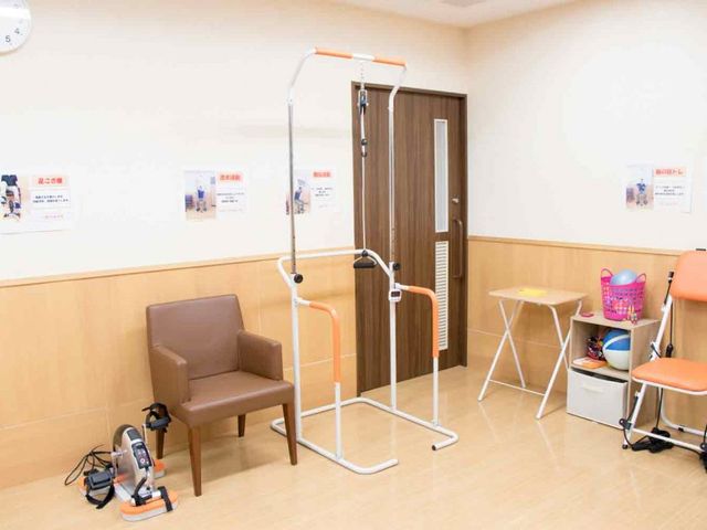 機能訓練器具のある部屋 機能訓練室 広々とした空間で、リハビリ機器を使った体力づくりが行えます。壁には運動の案内が掲示されています。