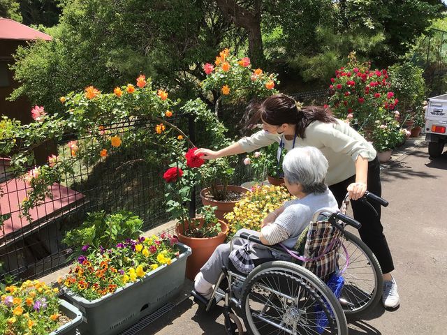 花に囲まれた庭 庭 色とりどりの花が咲く庭で、車椅子の方とスタッフが一緒に花を楽しんでいます。自然を感じる空間です。