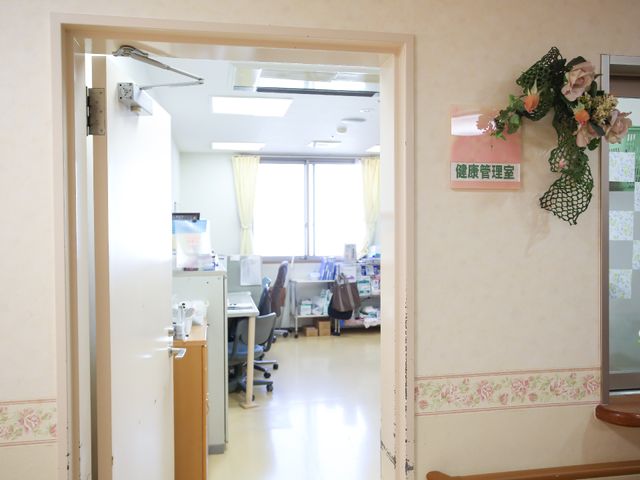 明るい事務所の入口 健康管理室 開放的な窓から日差しが差し込む快適な空間です。スタッフの協力的な雰囲気が伝わってきます。