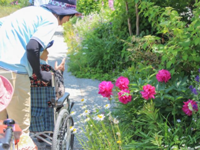 自然を楽しむ様子 庭 車椅子の利用者がスタッフと一緒に花を眺め、静かな庭でリラックスしています。