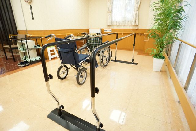 リハビリ用歩行器と車椅子 平行棒 明るい雰囲気の中で、歩行訓練に利用される機器が整っています。