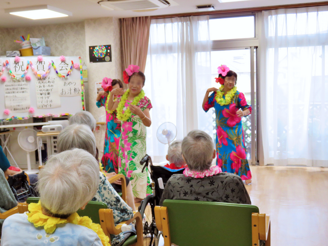 フラダンスのイベント風景 多目的室 衣装をまとった方々がフラダンスを披露しており、見守る皆さんの笑顔が印象的です。楽しいレクリエーションが充実しています。