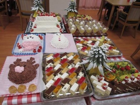 トナカイやサンタクロースのデコレーションケーキ、クリスマスツリーの形のカットフルーツが並んでいる。ケーキバイキングのイベント。