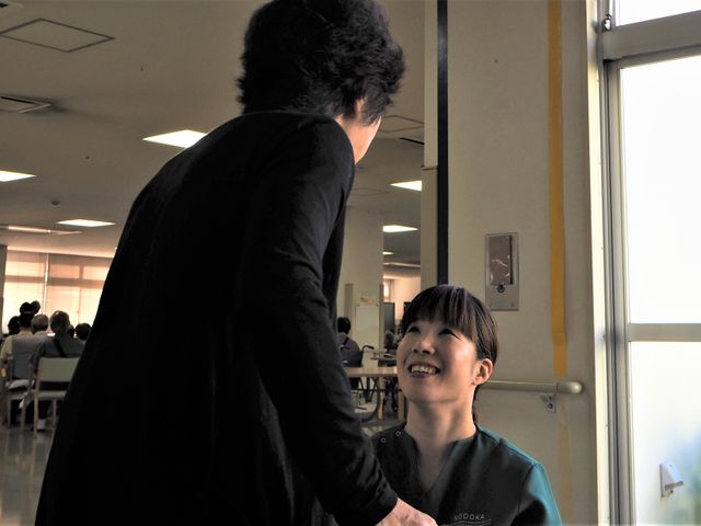 笑顔で会話するスタッフ スタッフと利用者の温かな会話の一コマです。明るい表情で対話を交わし、心地よい雰囲気が伝わって参ります。