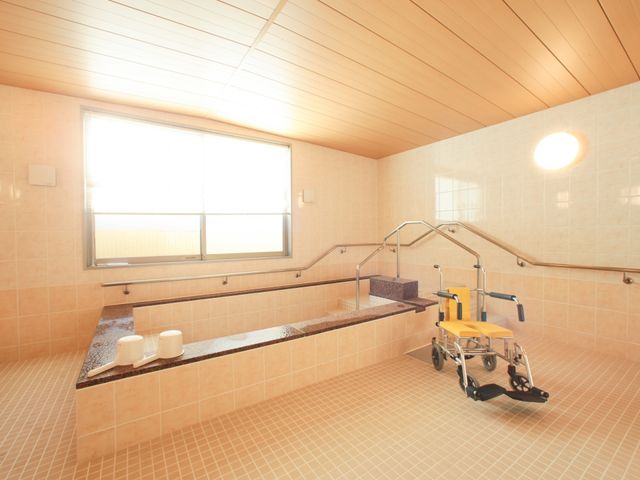 広々とした浴室の様子 浴室 天井が高く、明るい光が差し込む清潔感のある浴室です。手すりや椅子が整ったバリアフリー設計になっており、安心してご利用いただけます。