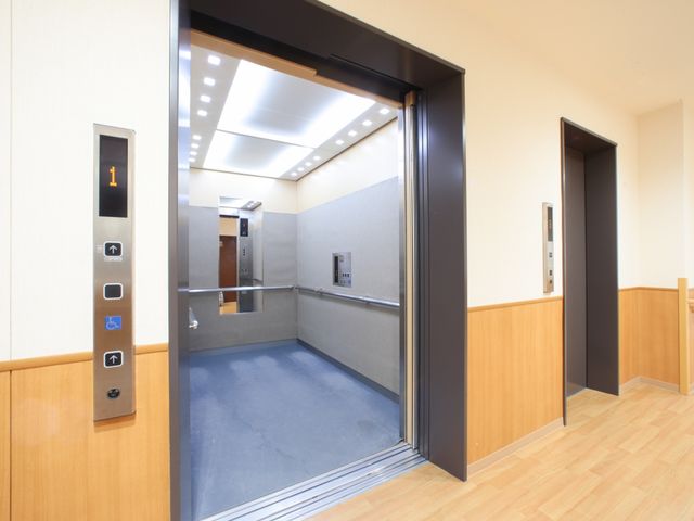 広々としたエレベーター空間 エレベーター 床や壁に木目調を採用したエレベーターは、明るく温かみのある雰囲気です。手すりが整備され、安全に配慮された設計となっています。