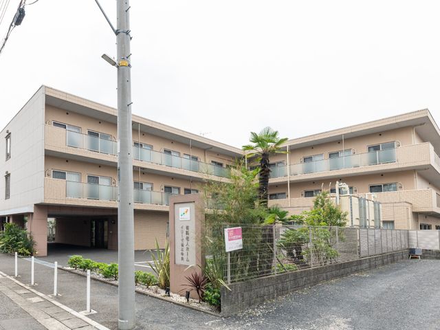 広々とした施設の外観 外観 落ち着いた色合いの建物が道路沿いに立っており、清潔感があります。エントランスまでの緩やかなアプローチは、訪れる方々へやさしい印象を与えるでしょう。