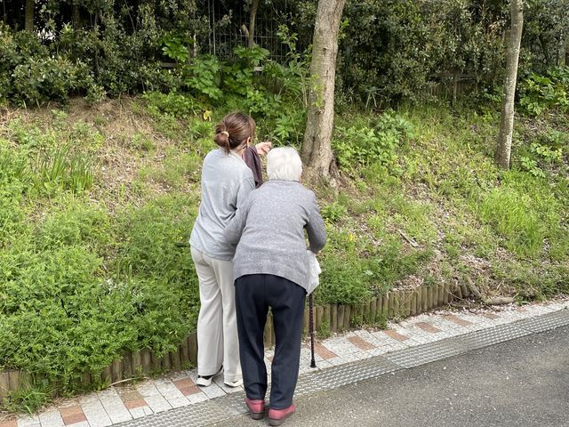 見守る介助者と緑道 外観 緑豊かな道を歩く様子が見られます。リラックスできる環境で、自然との調和を感じられます。