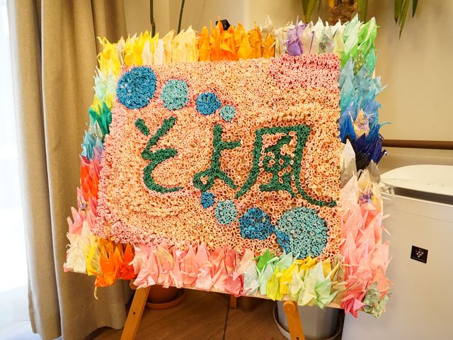 手作りのお祭り飾り 展示物 色とりどりの折り紙で作られた手作りの飾りが、来訪者や働く人たちを温かく迎えています。創造的な作業が活発な環境が垣間見えます。