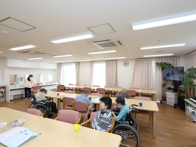 座って過ごす人々の共有空間 共有スペース 広々とした明るい空間で、入居者がリラックスしながら過ごしています。共有スペースでのコミュニケーションも活発に行われており、充実した日々を過ごせそうです。