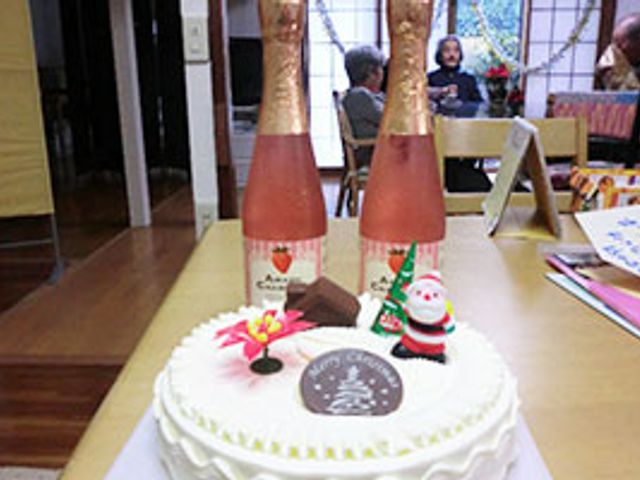 テーブルとケーキのある室内 洋室 テーブル上にクリスマスケーキが飾られた、温かみのある室内空間です。後方では人々が会話を楽しんでいます。