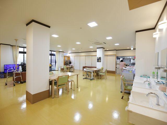 共用スペースの光景 食堂 落ち着いた雰囲気の多目的室です。居住者がリラックスして過ごせる挨拶交わすスタッフの姿も見られます。