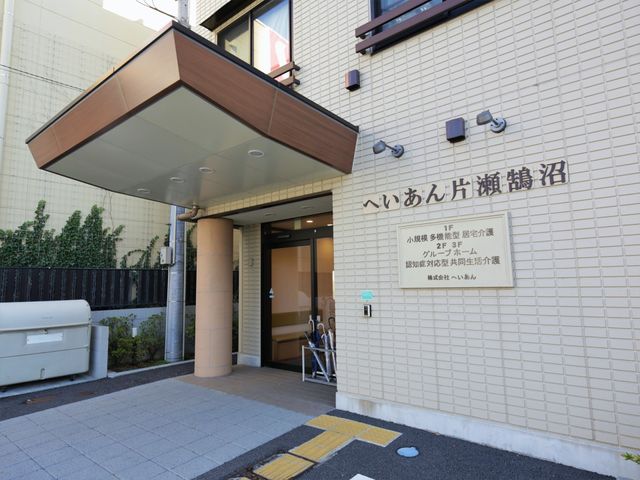 エントランス標識と玄関 外観 清潔で明るい入り口には、案内板が設置されており、訪れる方々への配慮が感じられます。周辺に緑があり、心地よい環境が提供されている様子です。