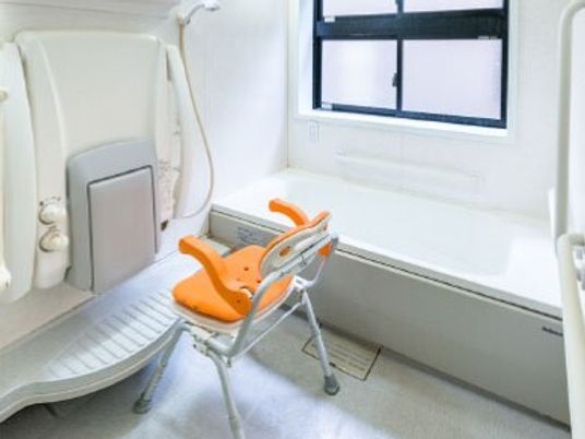 オレンジのシャワーチェアやシャワーが設置された浴室には、一人用の浴槽が設置され、手すりも付いている。
