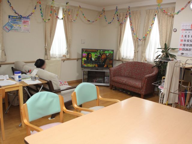 リビングの一角 リビング ゆったりとしたソファがあり、テレビを見ながらくつろげる暖かい雰囲気のリビングです。職員が作業中で、日常生活のサポート体制も整っています。