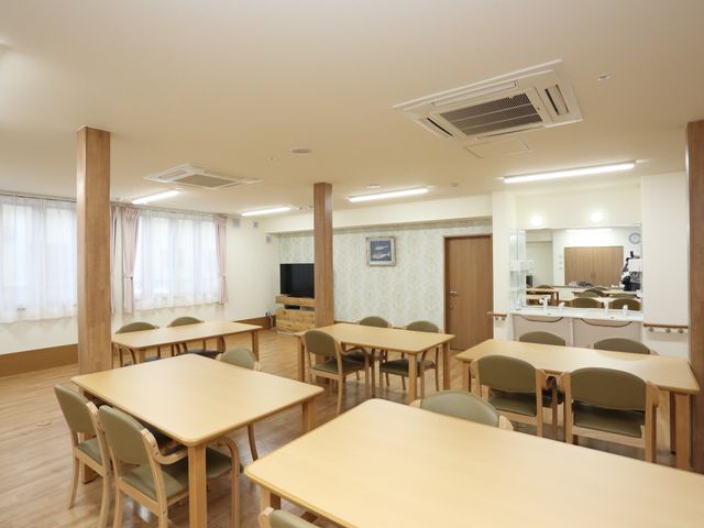 広々とした明るい食堂 リビング 木目調のテーブルが並ぶ食堂は、天井が高く開放感のある落ち着いた空間です。大画面のテレビも完備しており、食事の時間を快適に過ごせます。