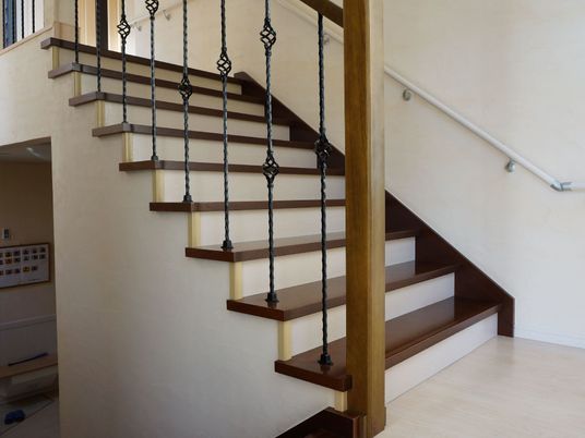 階段の踊り場からの風景。階段は白色がメインで、各段などはこげ茶色をしている。片方の手すりは鉄製で、装飾が施されている。
