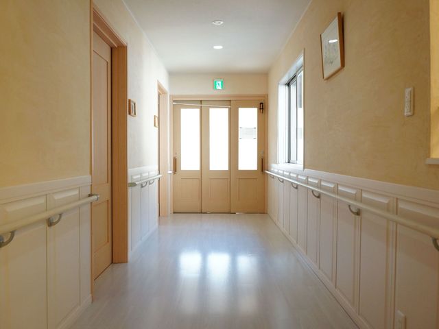 明るい廊下の様子 廊下 手すり付きで広々とした廊下は、どなたでも安心して歩ける環境を整えています。壁には絵画も飾られ、温かみのある空間です。