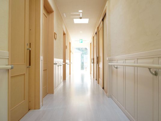 廊下がまっすぐ伸びている。廊下の両側には、居室のドアが並んでいて、ドアとドアの間には手すりが取り付けられている。