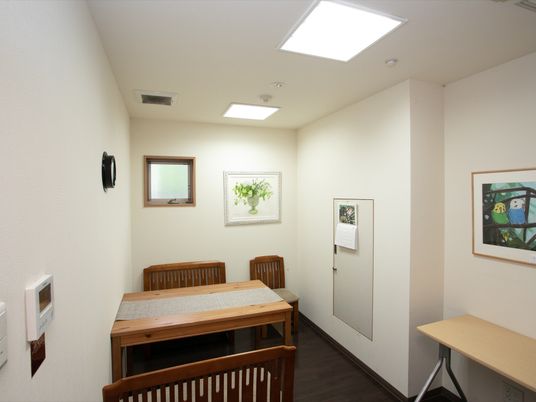相談室の壁に、額入りの絵が掛けられている。小さな換気窓が設置されている。木製のテーブルセットが配置され、テーブルランナーが敷かれている。