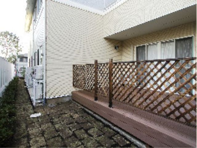 白壁の建物と緑の中庭 ウッドデッキ 手入れが行き届いた中庭は、潤いと静けさを提供してくれます。屋外での憩いの時間を愛する方にはぴったりの空間です。