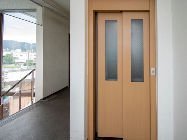 廊下の木製扉 エレベーター 明るい光が差し込む通路に面した扉で、落ち着いた色合いが特徴です。
