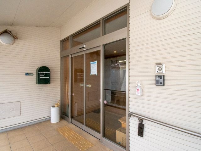 エントランスの明るい外観 玄関 清潔感のあるエントランスで、安心感を与える設計です。手指消毒剤の設置も見受けられます。