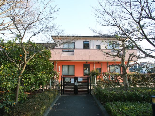 橙色の建物と緑濃い庭 外観 落ち着いた色合いの外観で、周囲には緑が多く植栽されています。自然に囲まれた環境で働きたい方に適しています。