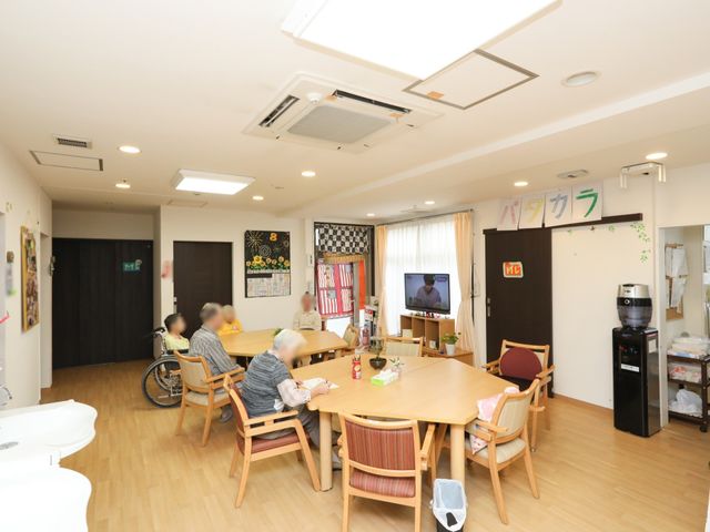 居心地の良い居室の様子 共有スペース 光が降り注ぐゆったりとした空間で、利用者の方々が心地よく過ごされています。柔らかな椅子と温かみのあるテーブルが配置された居室です。