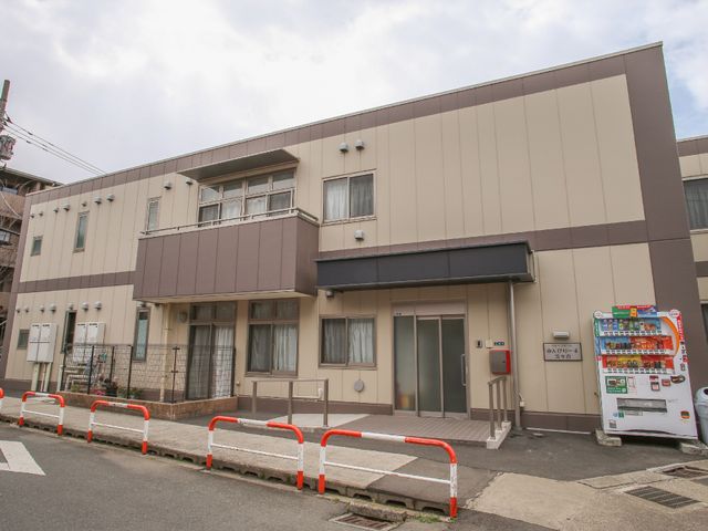 清潔感のある建物のエントランス 横長の施設 落ち着いた色合いのエントランスは、訪れる方を優しく迎え入れる設計になっており、入口には自動販売機も完備されています。