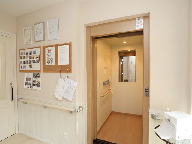 廊下の壁面情報掲示 開放感あふれるリビングルーム 壁には利用者さまのポートレートや情報が掲示され、アットホームな雰囲気を演出しています。廊下自体もバリアフリー設計になっております。