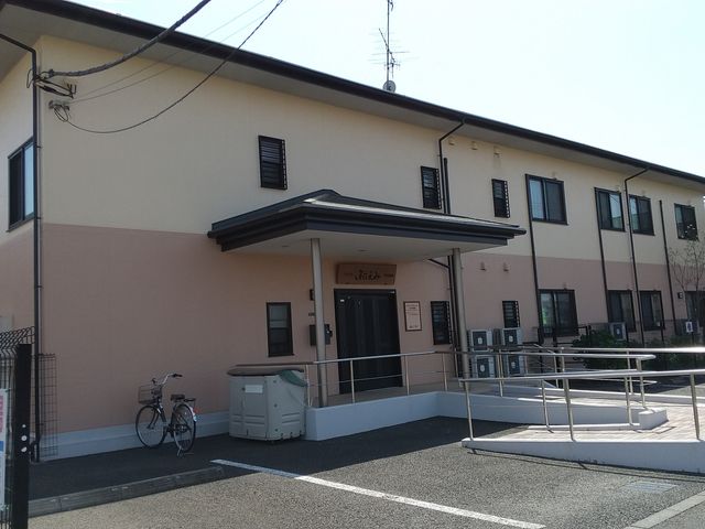 建物の外観です 外観   落ち着いた色合いの2階建てで、正面に屋根付きの出入口があります。車椅子でも通りやすそうなスロープがあり、働く場としても動線を確認しやすい印象です。