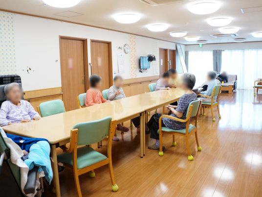 天井には多数のライトが設置され、一側面がガラス戸になっている明るい空間には、中央に長いテーブルあり、多数の入居者様が座っている。