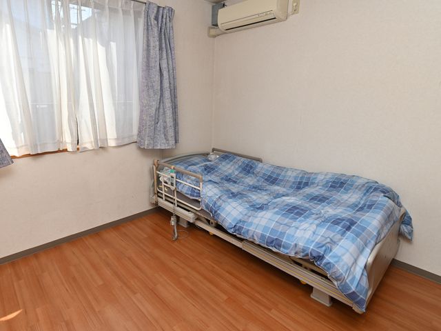 清潔な居室の一角 居室 窓際に設置されたベッドは、日差しを取り入れた明るい雰囲気を感じさせます。エアコン付きで快適な居住空間が確保されています。
