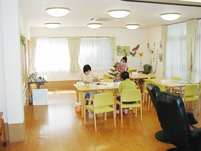 明るい共用ダイニング空間 ダイニング 木目調の家具を配した温かみのあるダイニングで、来訪者が食事をとる様子がご覧になれます。スタッフのサポートも見受けられ、ゆったりとした時間が流れています。
