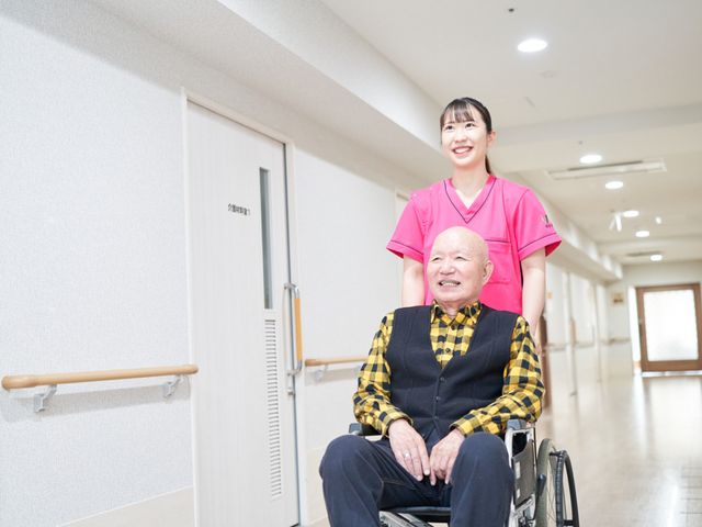 広い廊下 廊下 車椅子での移動が楽な、清潔で明るい廊下です。職員が笑顔でサポートしています。