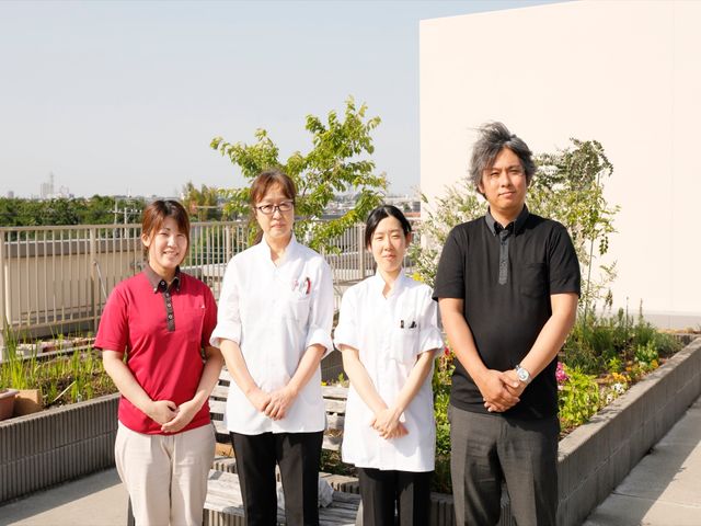 スタッフ立つ中庭 スタッフ 中庭には明るい陽光の下、笑顔で立つスタッフがいて、共に働くあたたかな雰囲気が伝わってきます。チームワークを大切にし、居心地の良い環境作りに取り組んでいます。