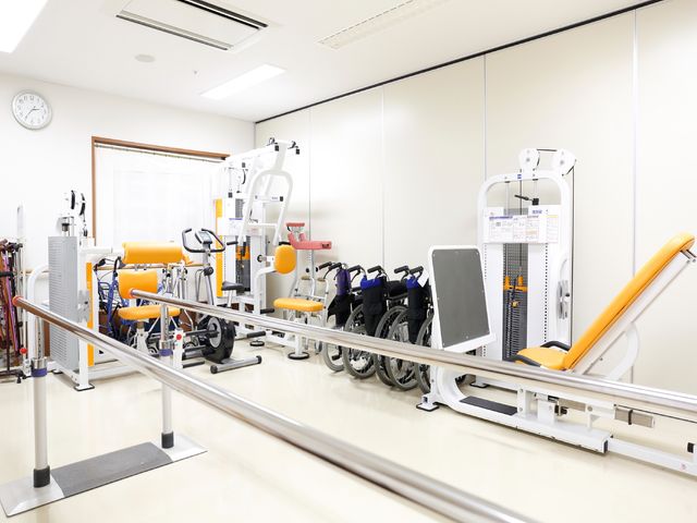 様々なリハビリ機器のある部屋 運動室 充実した機能訓練機器が揃った広々とした空間で、日々のリハビリテーションをサポートいたします。患者様の身体能力向上を助けるために、多様な機器が整っております。