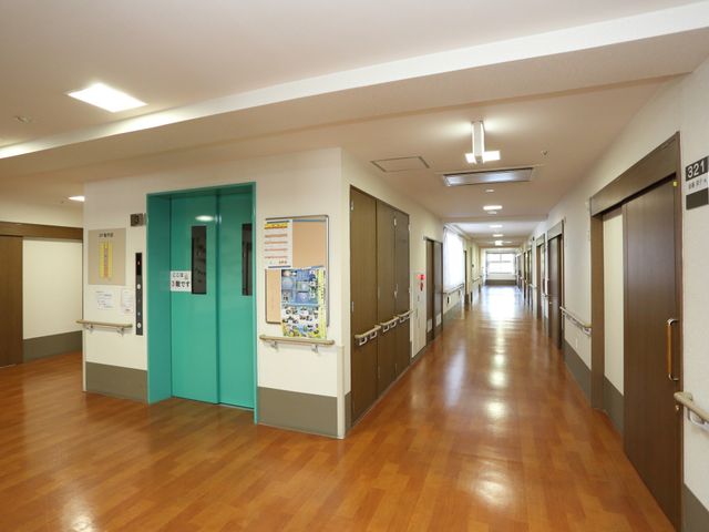 清潔な廊下と案内掲示 廊下 光が差し込む廊下は清潔感があり、壁には案内表示や掲示物があります。ゆったりと歩ける広々とした空間が確保されています。