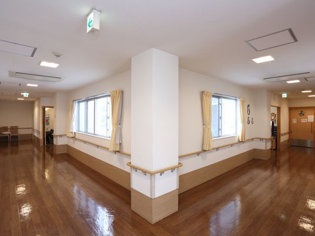 広々とした明るい廊下 通路 ゆったりとした通路が確保されており、日差しの差し込む窓辺では穏やかな時間を過ごせる様子です。手すりも設置され、安全に配慮された空間になっています。