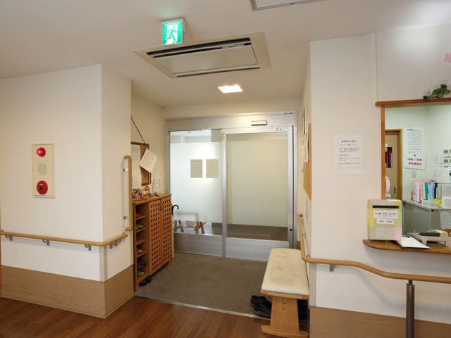 出入口付近の通路 玄関受付 手すりが設けられた明るいエントランスです。受付付近には情報掲示があり、訪れる方が必要な情報を容易に得られるようになっています。