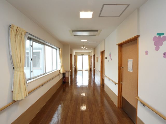 明るく清潔な廊下 通路 広々とした廊下は木目調のフローリングで、壁には楽しげなデコレーションが施されており、温もりを感じさせる空間です。手すりも完備され、安心して歩行できるよう工夫がされています。