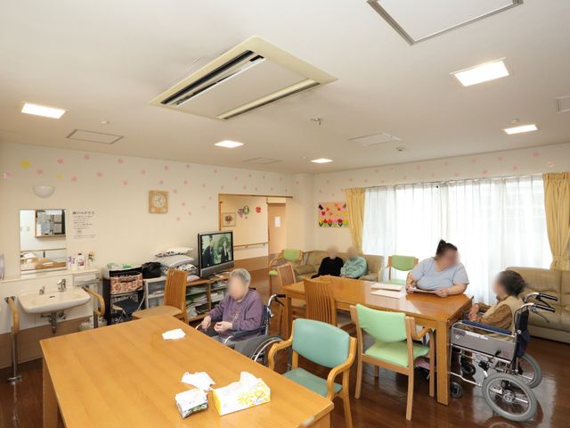 共有空間の居心地の良さ 談話室 様々なアクティビティが楽しめる明るいリビングです。利用者様がソファやテーブルを囲んでくつろいでおり、和やかな雰囲気が漂っています。