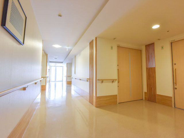 明るく清潔な廊下 出入口周辺 床が光を反射して明るい廊下で、手すりが設置されています。歩行に不安のある方も安心して移動できる設計です。