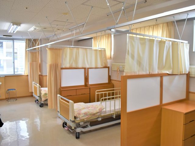 穏やかな居室の一角 居室 木製のパーティションで区切られた清潔感のあるベッドスペースです。陽だまりのような心地よさを感じていただける空間です。