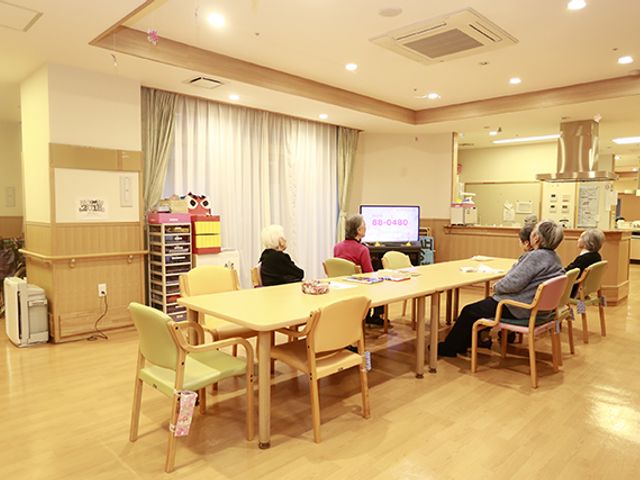 明るい共有スペース ラウンジ 自然光が入る明るい空間で、入居者の皆さんが和やかにテレビを見ながら過ごされています。