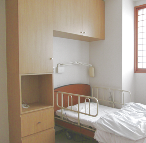 静かな居室のベッド 居室 落ち着いた雰囲気の居室で、木製の収納と大きな窓が備わっています。リラックスできる空間です。