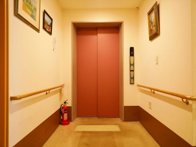 暖かみのあるエレベーター前 エレベーター 廊下の終わりに位置し、手すりが整ったエレベーター前です。通路はゆとりがあり、すべての方が安全に利用できる設計になっています。